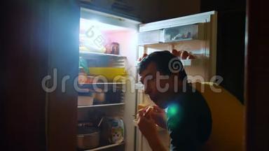 人们晚上从冰箱里吃饥饿和饕餮。 男人晚上看冰箱的生活方式。 饕餮